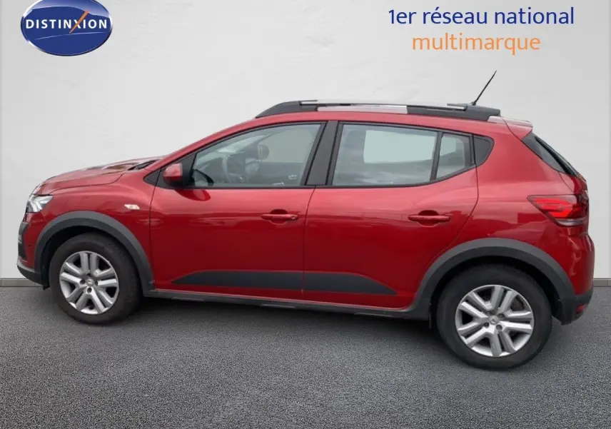 Vue de profil côté gauche d'une Dacia Sandero Stepway rouge fusion métal avec barres de toit et protections noires.