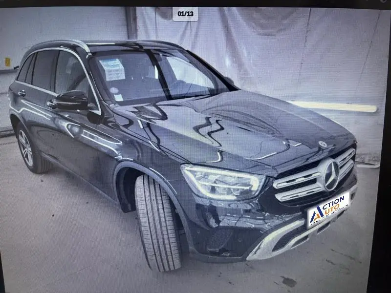 Vue 3/4 avant droit d'un Mercedes GLC noir avec calandre chromée et phares LED allumés dans un garage.