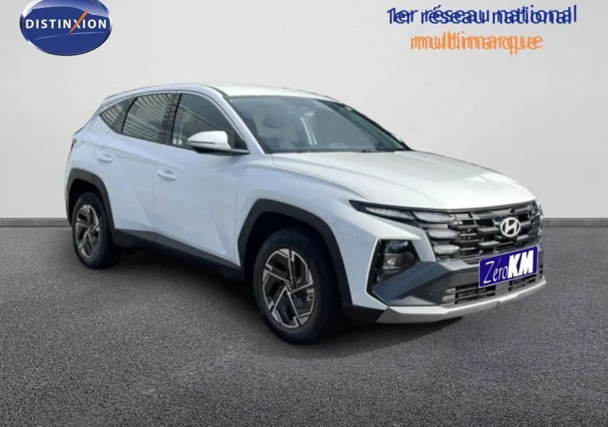 Hyundai Tucson blanc atlas vu en 3/4 avant droit, avec calandre marquée et jantes bi-ton distinctives.