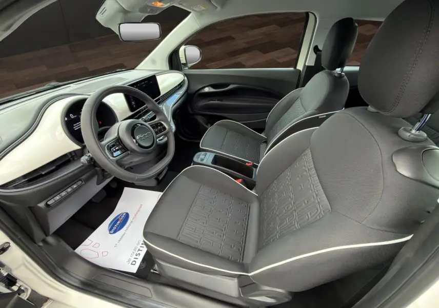Vue intérieure côté conducteur de la Fiat 500 blanche 2023, avec tableau de bord blanc brillant et sièges gris à surpiqûres blanches.