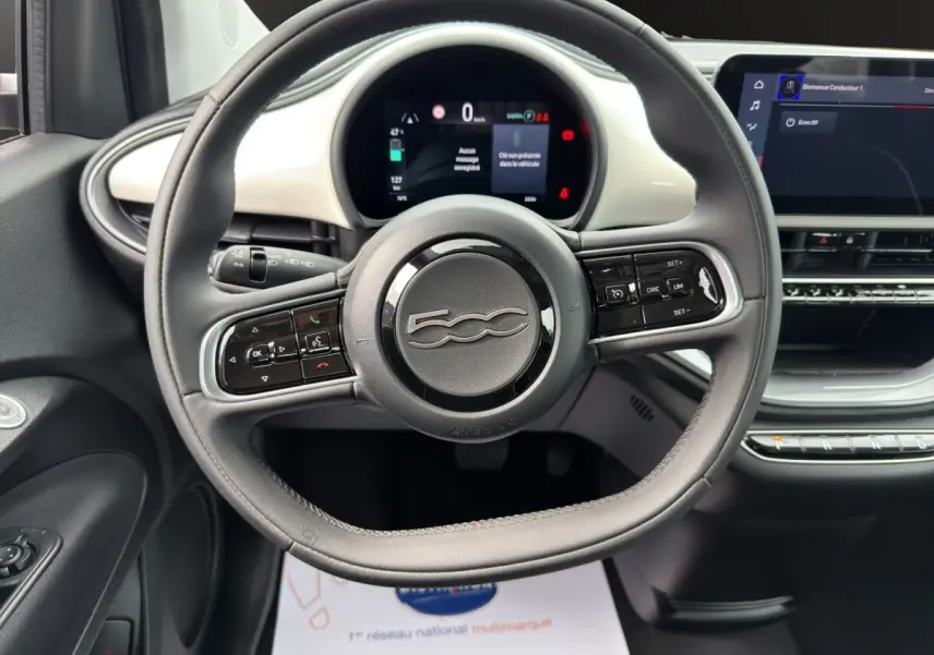 Vue rapprochée du volant cuir noir et du tableau de bord blanc de la Fiat 500 électrique 2023 avec écran tactile central.