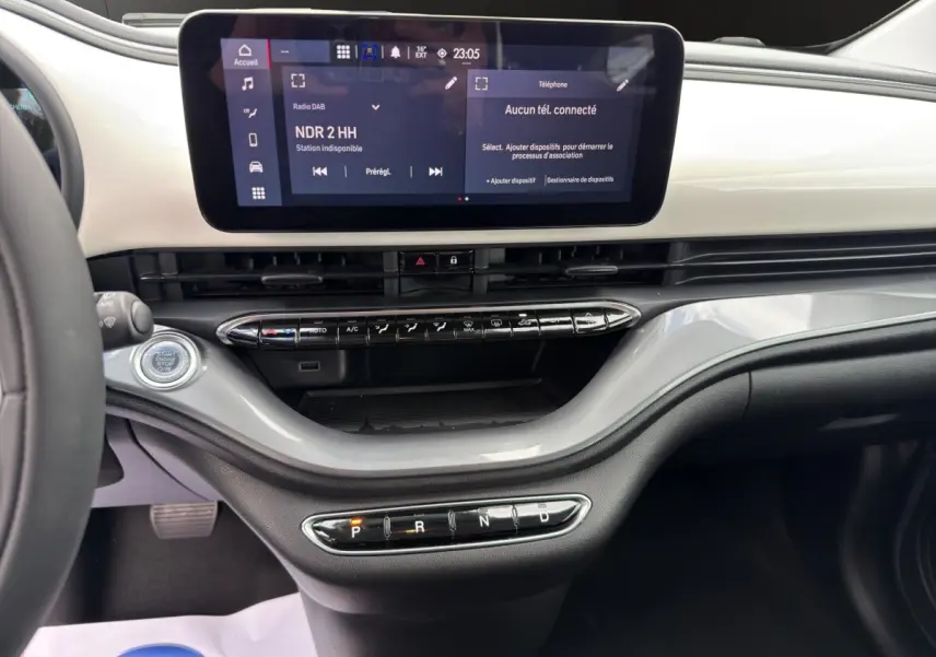 Vue intérieure du tableau de bord de la Fiat 500 blanche, avec écran tactile central et commandes de climatisation.