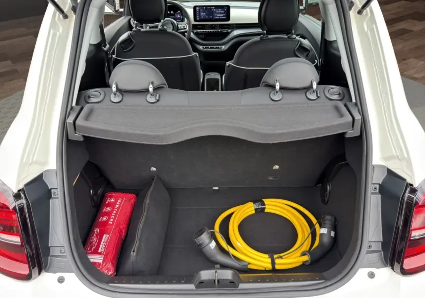 Coffre ouvert d'une FIAT 500 blanche vue de l'arrière, avec câble de charge jaune et trousse de secours rouge visibles.