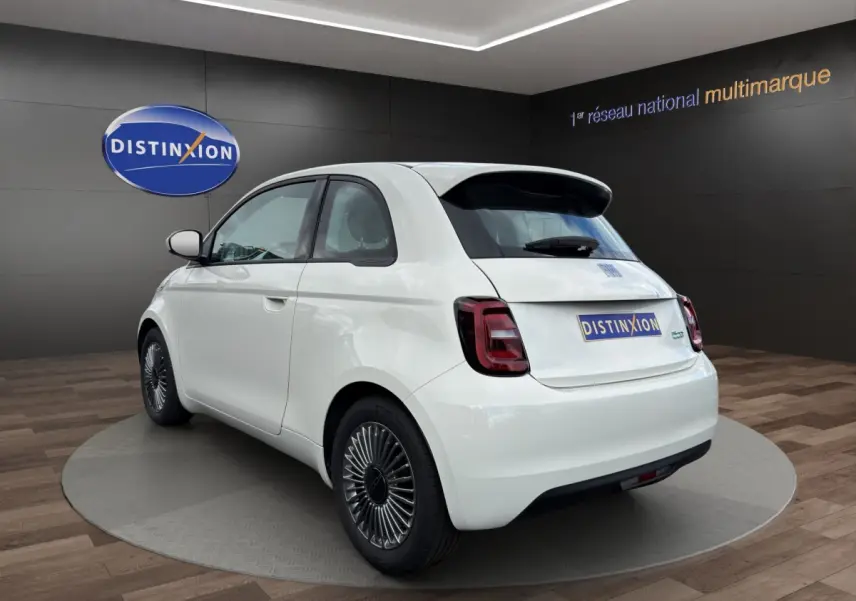 Vue 3/4 arrière droite d'une FIAT 500 électrique blanche avec jantes alu spécifiques et toit noir contrasté.