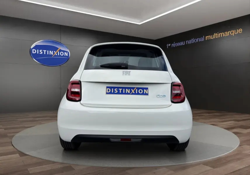 Vue arrière d'une Fiat 500 blanche électrique 2023 dans un showroom avec logo Distinxion en arrière-plan.