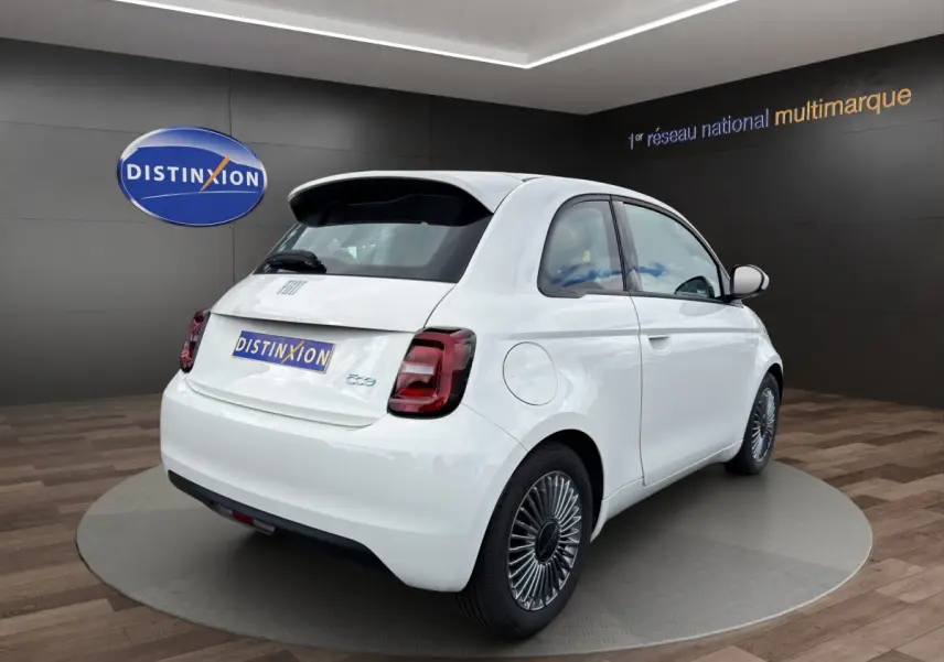 Vue 3/4 arrière droite d'une FIAT 500 électrique blanche avec jantes alu stylisées en exposition showroom.