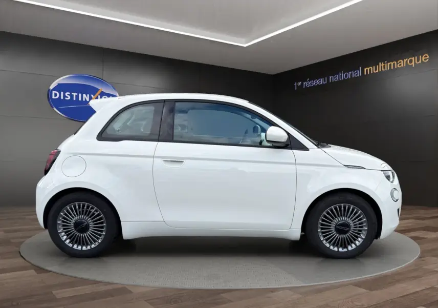 Profil droit de la FIAT 500 électrique blanche 2023 avec jantes alu et toit spoiler en showroom.