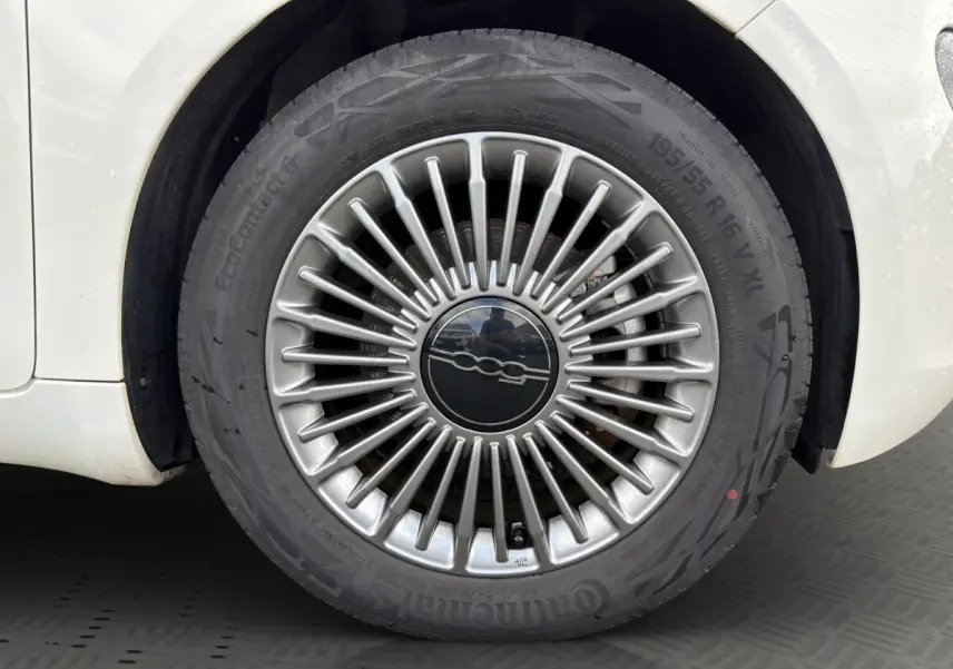 Gros plan sur la jante alu argentée au design rayonné d’une FIAT 500 blanche électrique, côté arrière droit.