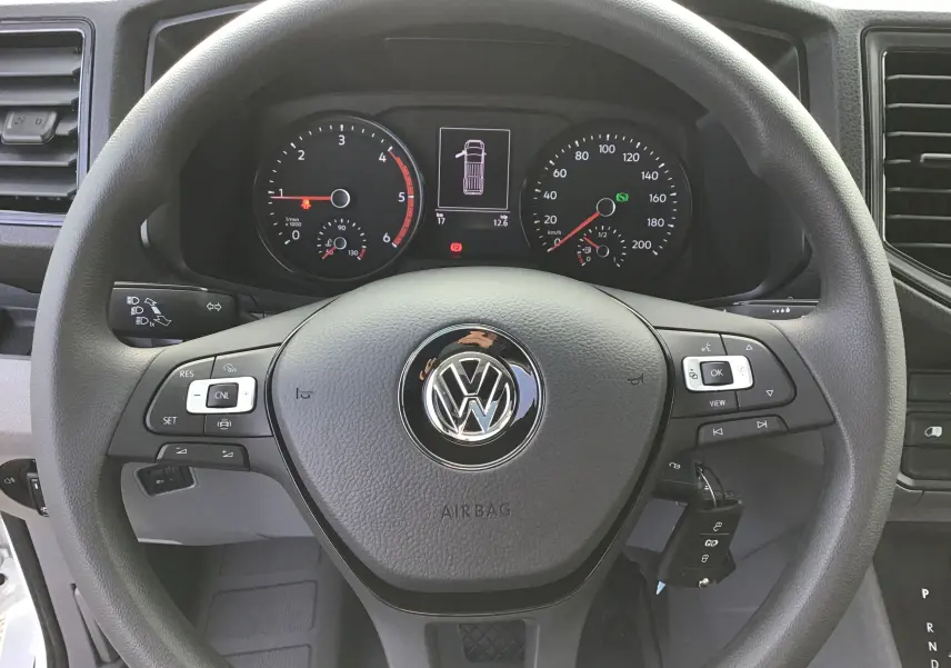 Vue rapprochée du volant noir et du tableau de bord du Volkswagen Crafter Fourgon blanc 2024 avec commandes au volant.