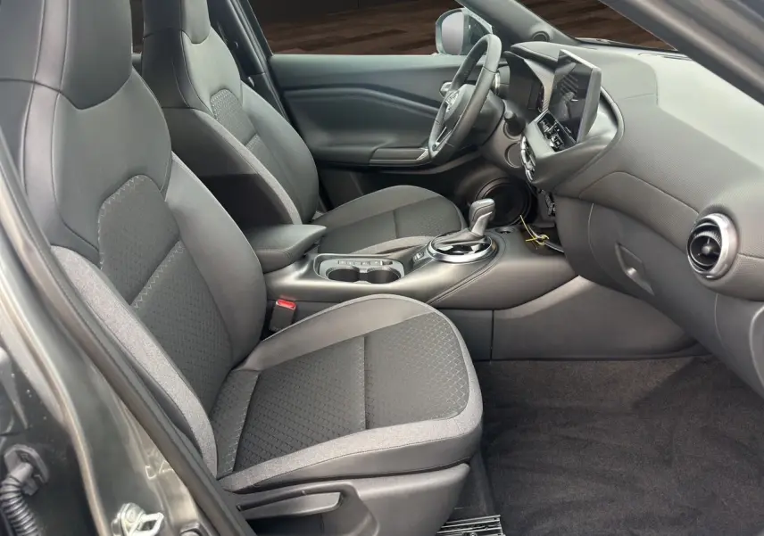 Intérieur avant du Nissan Juke Full Hybrid 2025, vue côté gauche, sièges tissu noir et console centrale moderne.