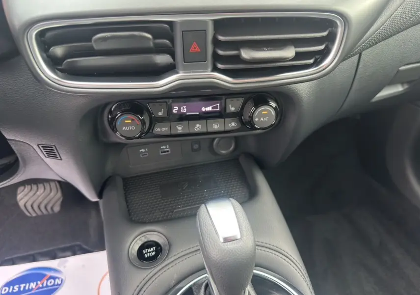 Gros plan sur la console centrale du Nissan Juke gris, montrant la commande de climatisation et le levier de vitesse automatique.