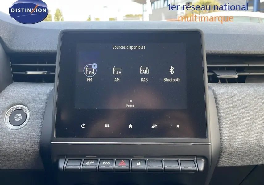 Vue intérieure centrée sur l'écran tactile multimédia de la Renault Clio gris schiste métal, avec bouton Start Engine Stop visible.