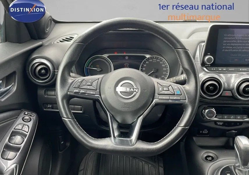 Vue intérieure centrée sur le volant cuir noir du Nissan Juke Hybrid 2023 avec tableau de bord et écran tactile visibles.