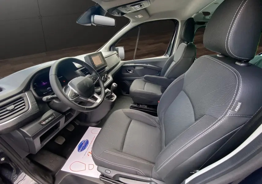 Intérieur avant du Renault Trafic gris comète, vue côté conducteur, sièges noirs avec coutures blanches et tableau de bord moderne.
