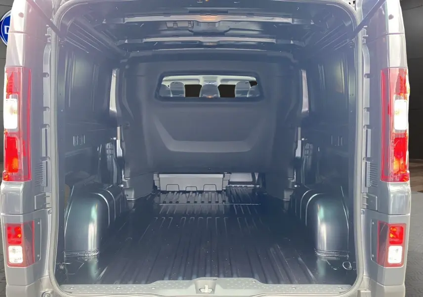 Vue arrière du Renault Trafic cabine approfondie gris comète, montrant l'espace de chargement vide et les feux arrière allumés.