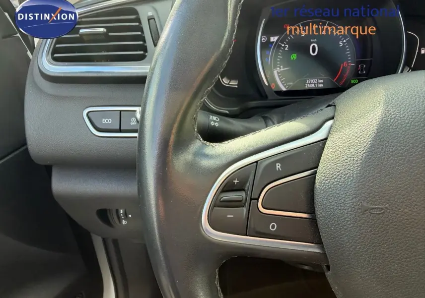 Gros plan sur le volant noir et le tableau de bord numérique du Renault Kadjar blanc nacré, avec boutons de commande visibles.
