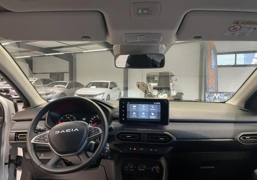 Vue intérieure avant du tableau de bord noir et volant DACIA avec écran tactile central allumé.