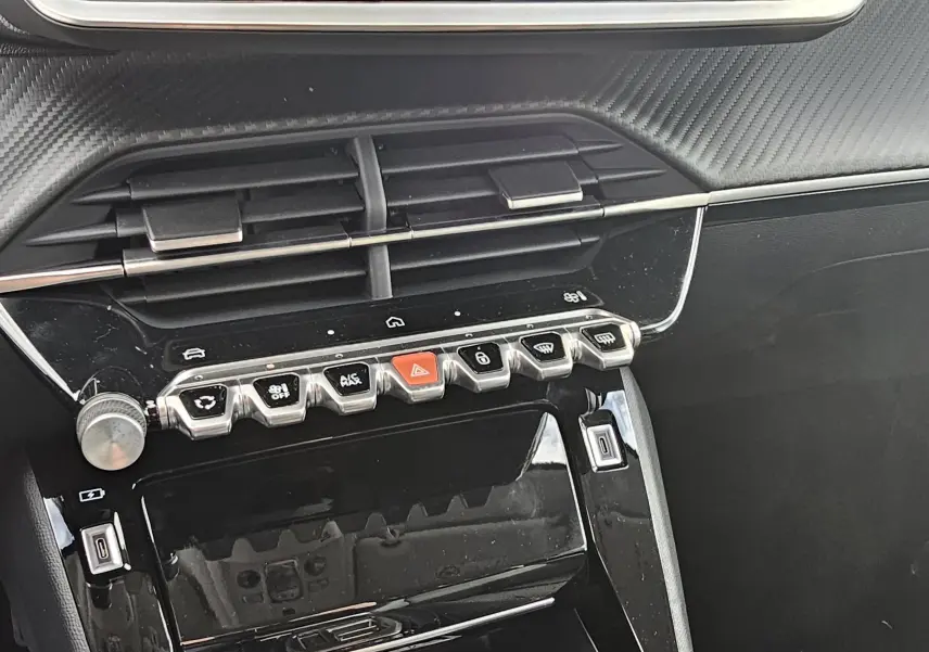 Détail de la console centrale noire brillante de la Peugeot 208 110 hybrid Allure avec boutons de commande et aérateurs.