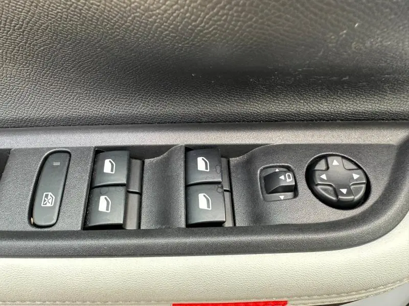 Gros plan sur les commandes de lève-vitres et réglages des rétroviseurs côté conducteur d'une Citroën C3 noire.