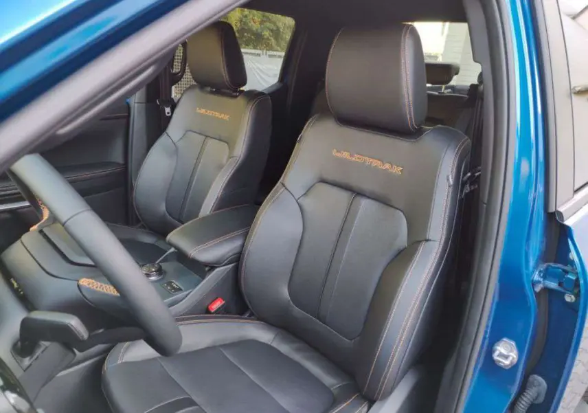 Vue intérieure côté conducteur du Ford Ranger Wildtrak 2025 bleu lightning, sièges cuir noirs avec surpiqûres orange et logo Wildtrak.
