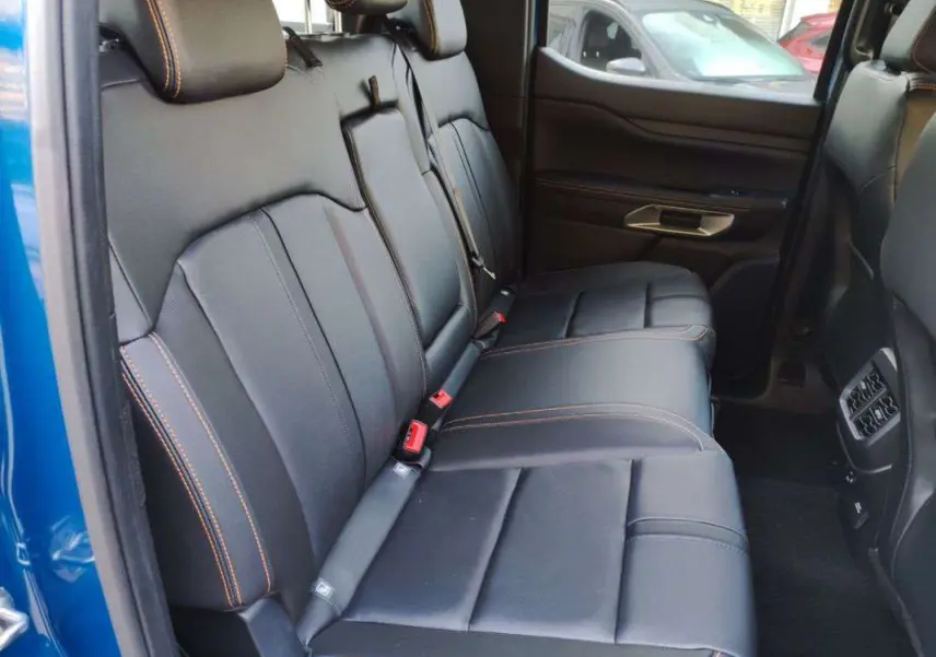 Vue intérieure côté gauche des sièges arrière en cuir noir avec surpiqûres orange du Ford Ranger 2025 bleu lightning.