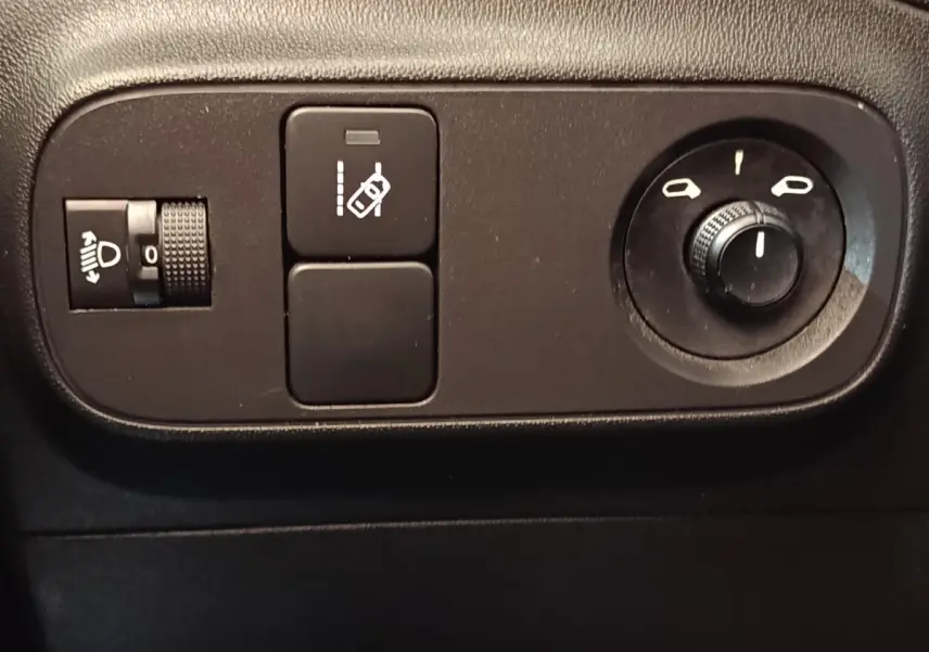 Gros plan sur les commandes intérieures noires du tableau de bord de la Citroën C3 blanche, avec réglage des phares et des rétroviseurs.