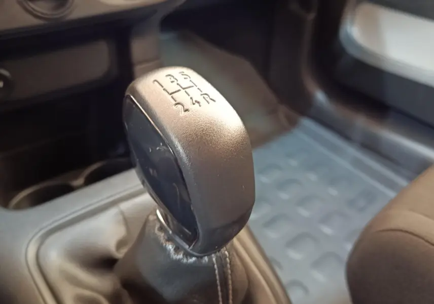 Gros plan sur le levier de vitesses manuel noir de la Citroën C3 blanche, intérieur avec tapis caoutchouc gris.