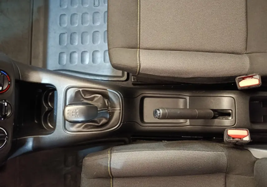 Vue de dessus de la console centrale noire avec levier de vitesse manuel et frein à main entre deux sièges tissu gris du Citroën C3 blanc.