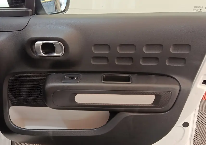 Vue intérieure de la porte avant gauche d'une Citroën C3 blanche, avec poignée chromée et panneau noir texturé.