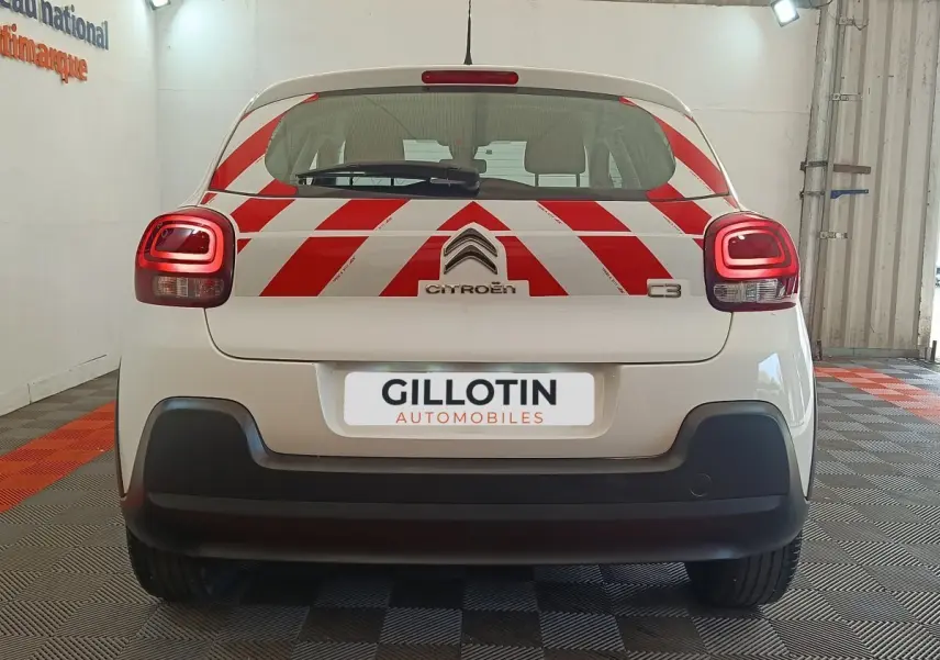 Vue arrière d'une Citroën C3 blanche 2021 avec marquages rouges en chevrons et feux arrière allumés en intérieur.