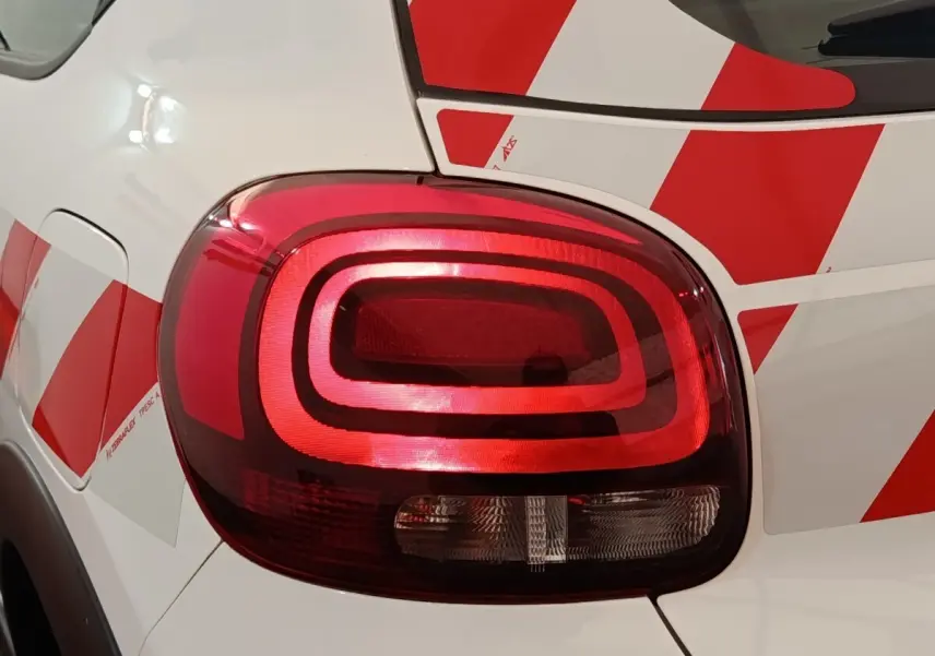 Gros plan sur le feu arrière droit rouge d'une Citroën C3 blanche avec motifs rouges géométriques.