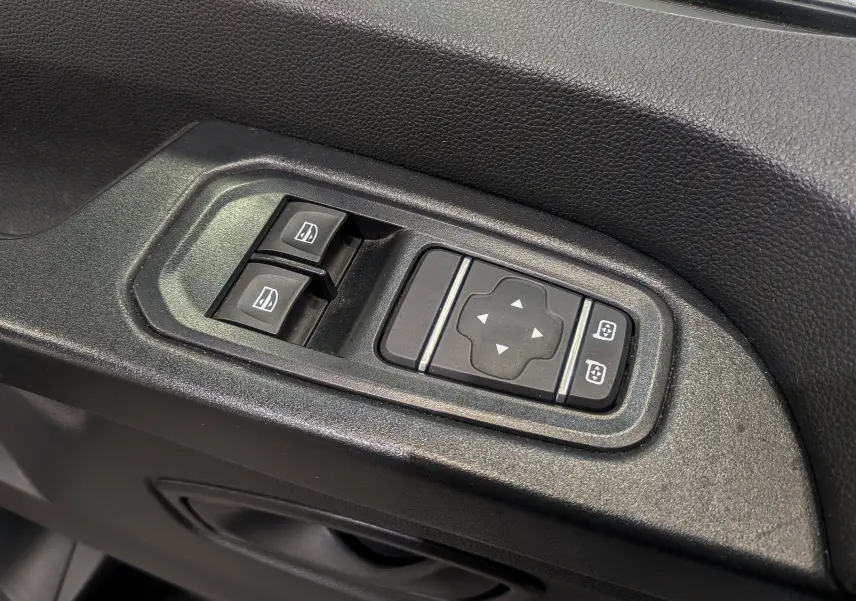 Gros plan sur les commandes de lève-vitres et réglage des rétroviseurs côté conducteur du Renault Trafic Fourgon blanc.