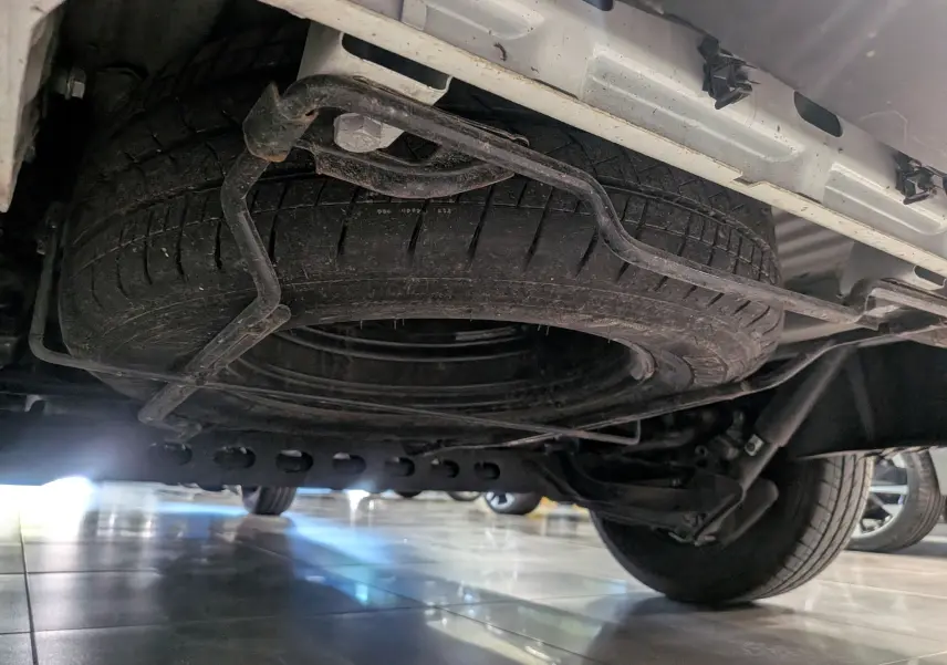Vue en contre-plongée sous un Renault Trafic Fourgon blanc minéral, montrant la roue de secours fixée sous le véhicule.