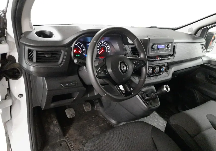 Vue intérieure côté conducteur du Renault Trafic Fourgon blanc, montrant le tableau de bord, volant et levier de vitesses manuel.