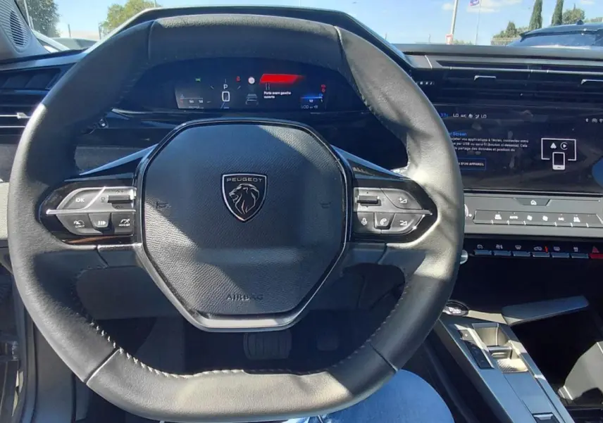 Vue intérieure centrée sur le volant Peugeot 308 gris, avec cockpit numérique et écran tactile de la console centrale.