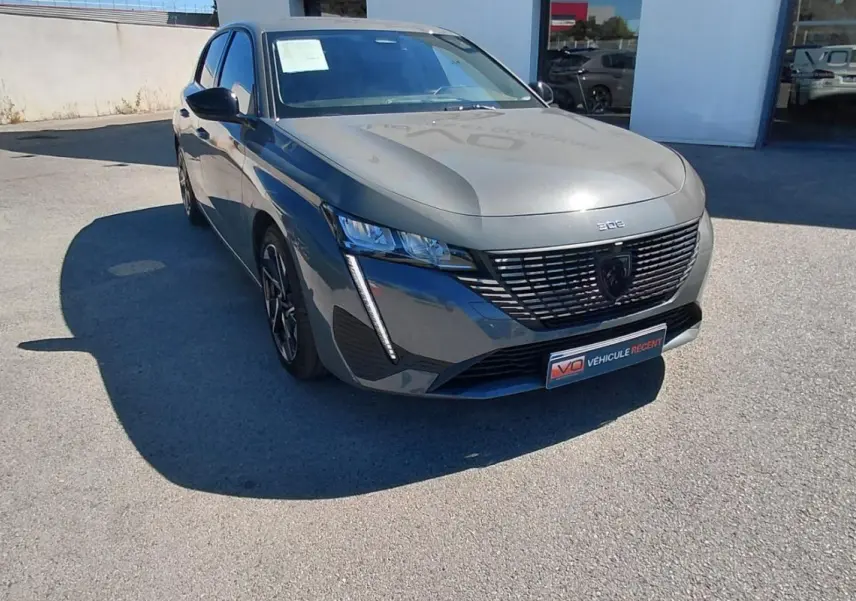 PEUGEOT 308 gris en 3/4 avant droit, avec calandre noire distinctive et jantes alliage 17 pouces visibles.