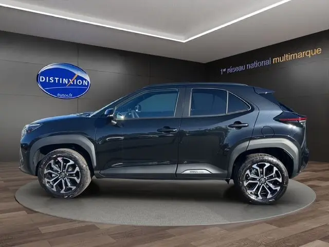 Profil côté gauche de la Toyota Yaris Cross 130H Design 2025 noire, avec jantes alliage et protections latérales visibles.