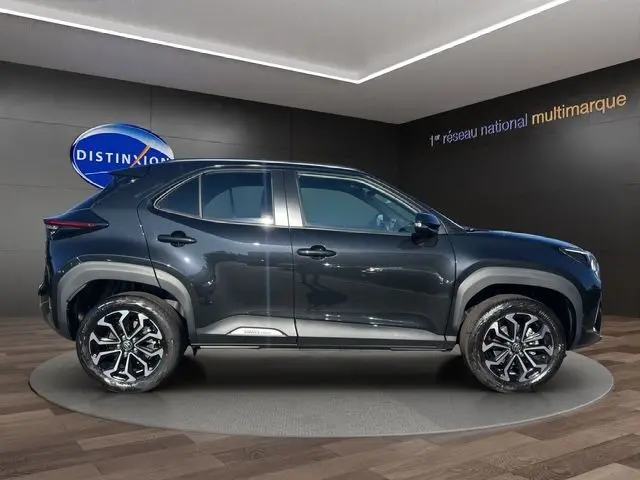 Profil côté gauche d'une Toyota Yaris Cross 130H Design noir brillant avec jantes alliage, en showroom.