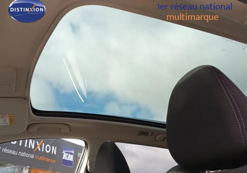 Vue intérieure du toit ouvrant panoramique du Nissan Qashqai blanc, avec appuie-tête avant en tissu noir visible.