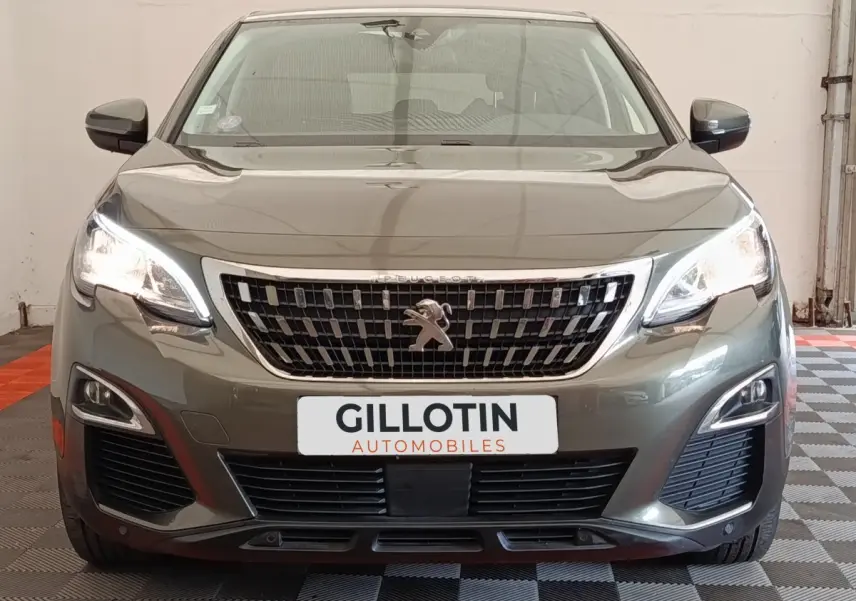 Vue frontale d'un Peugeot 5008 gris foncé avec calandre chromée et feux LED allumés dans un garage.