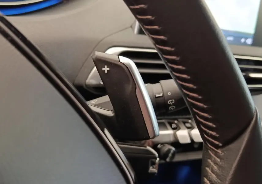 Gros plan sur la palette de changement de vitesse + au volant cuir du Peugeot 5008 gris foncé, intérieur moderne.