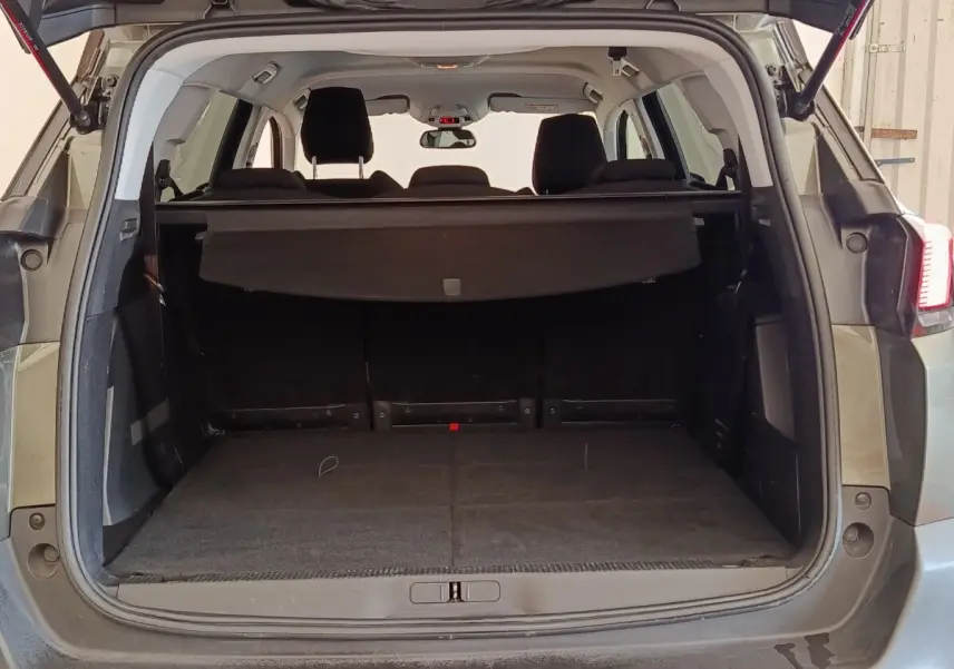 Vue arrière du coffre ouvert d'un Peugeot 5008 gris foncé, avec cache-bagages et sièges arrière visibles.