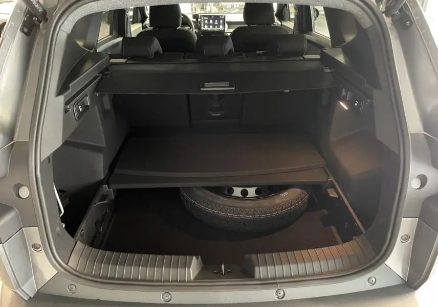 Vue arrière du coffre ouvert du Dacia Bigster gris schiste, montrant la roue de secours et la tablette de rangement.
