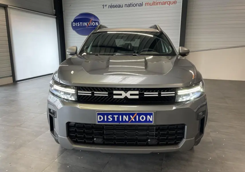 Vue frontale du Dacia Bigster gris schiste avec calandre noire et feux LED allumés en intérieur showroom.