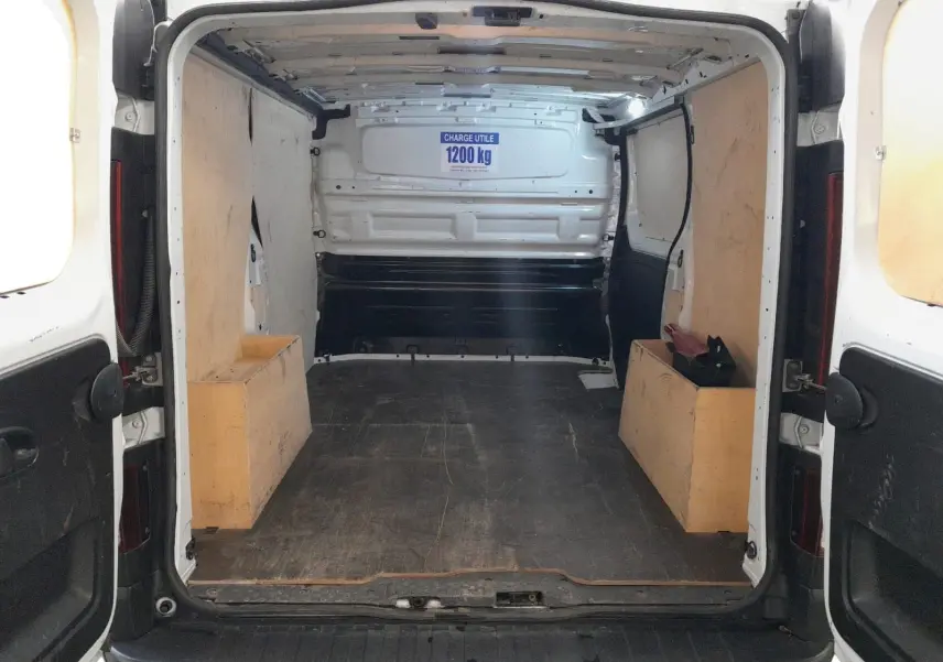Vue arrière ouverte du Renault Trafic Fourgon blanc minéral 2024, montrant l’espace de chargement avec panneaux en bois et capacité 1200 kg.