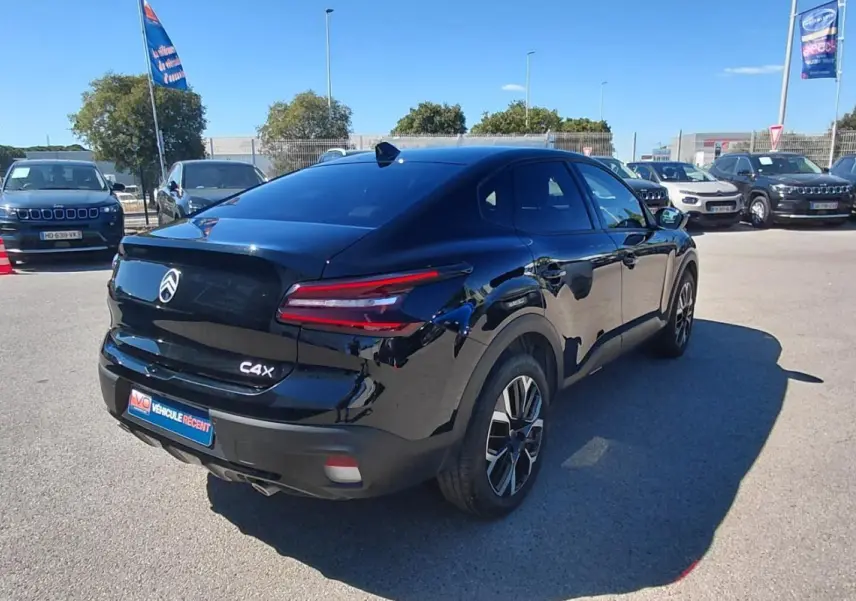 Vue 3/4 arrière droite d'une Citroën C4 X noire avec jantes alliage 17 pouces sur parking ensoleillé.