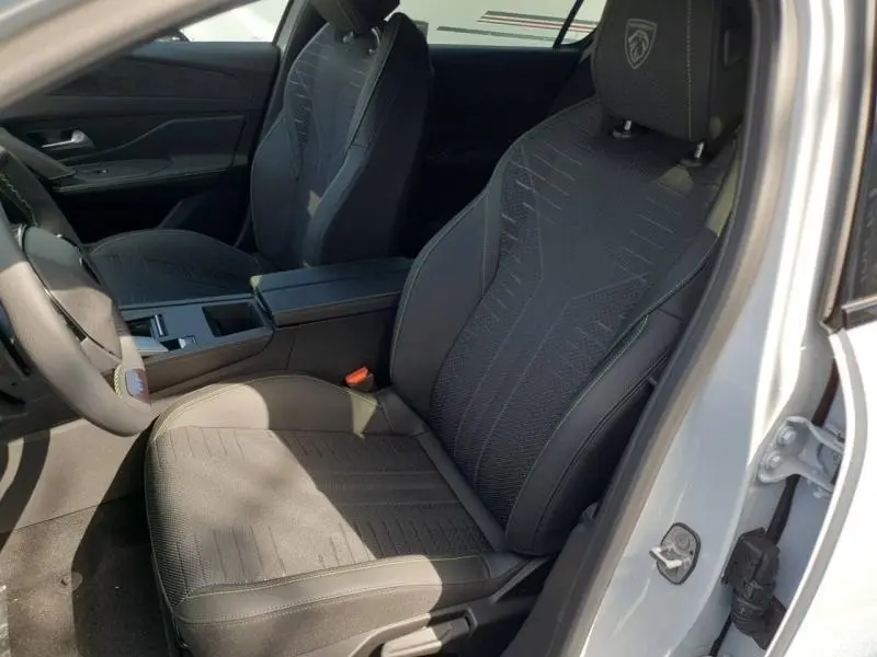 Vue intérieure côté conducteur de la Peugeot 308 Hybrid 2026, sièges noirs avec logo Peugeot brodé sur appuie-tête.