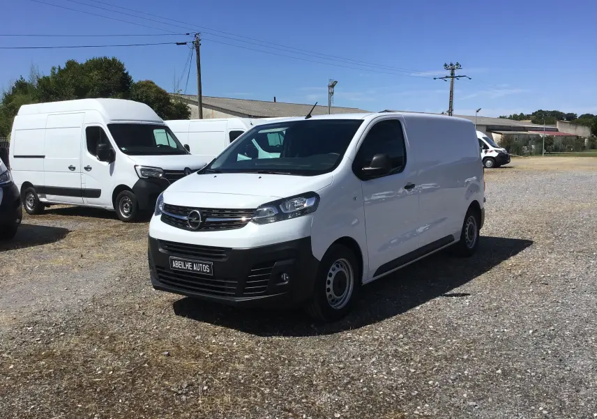 Vue 3/4 avant droite d'un Opel Vivaro blanc 2023 avec calandre noire et plaque Abeille Autos visible.