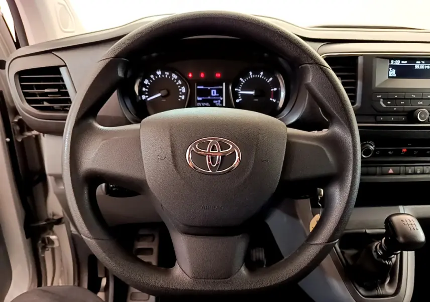 Vue intérieure centrée sur le volant noir du Toyota Proace Verso 2019 avec tableau de bord et levier de vitesses manuel visibles.