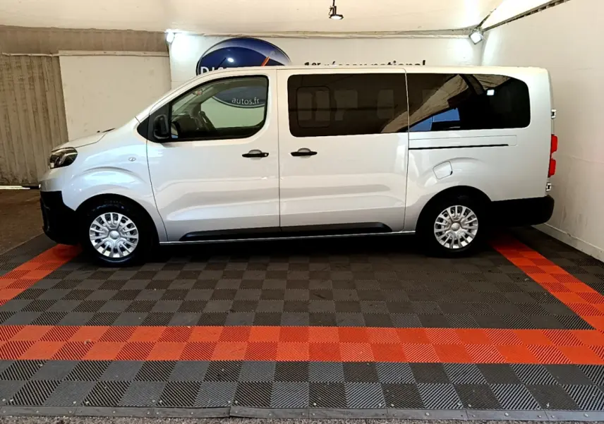 Profil côté gauche d'un Toyota Proace Verso gris clair avec vitres arrière teintées dans un garage.